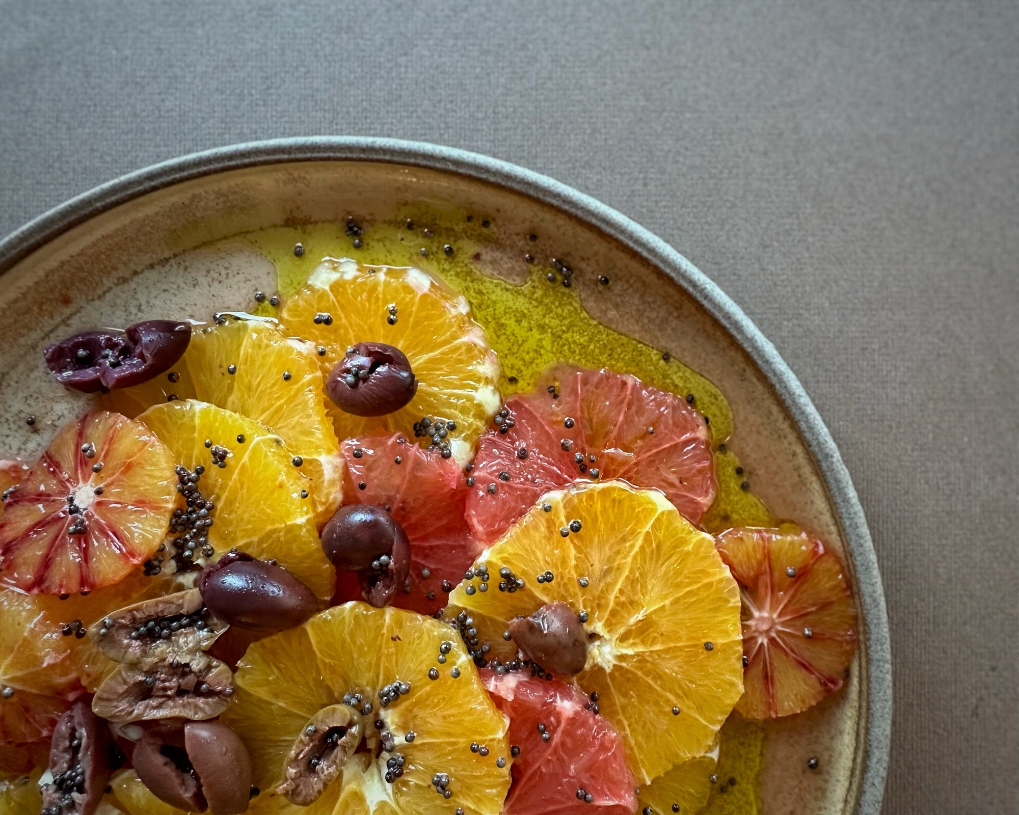 Winter citrus slices on a shallow ceramic plate, topped with mustard seeds and black olives.